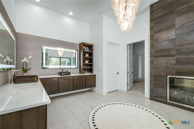 bathroom with vanity, a notable chandelier, a fireplace, tile patterned flooring, and a high ceiling