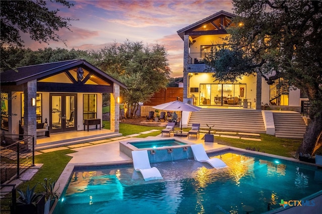 pool at dusk featuring an in ground hot tub, an outbuilding, and a patio