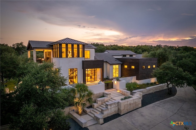 back of house at dusk with metal roof, a standing seam roof, concrete driveway, and stucco siding