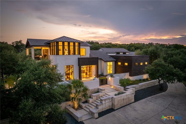 115 Steeplechase, New Braunfels, TX 78132 - back of house at dusk with metal roof, a standing seam roof, concrete driveway, and stucco siding