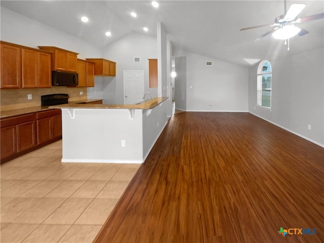 kitchen featuring black appliances, a kitchen breakfast bar, lofted ceiling, ceiling fan, and light hardwood / wood-style flooring