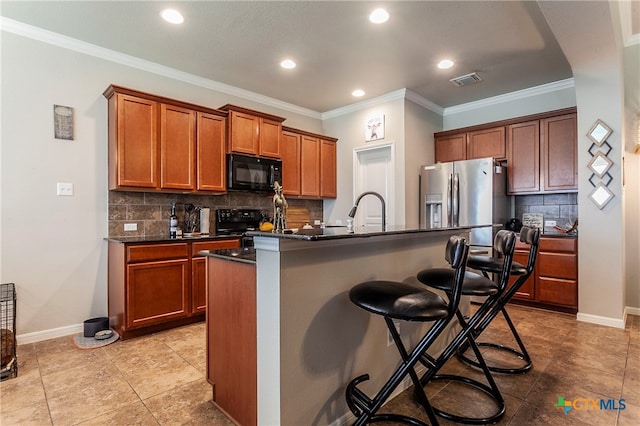 kitchen with a center island with sink, black appliances, ornamental molding, a breakfast bar area, and decorative backsplash