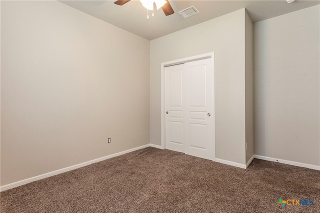 unfurnished bedroom with dark colored carpet, ceiling fan, and a closet