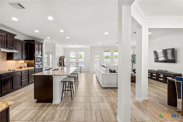 kitchen featuring stainless steel appliances, a kitchen breakfast bar, light stone countertops, backsplash, and an island with sink