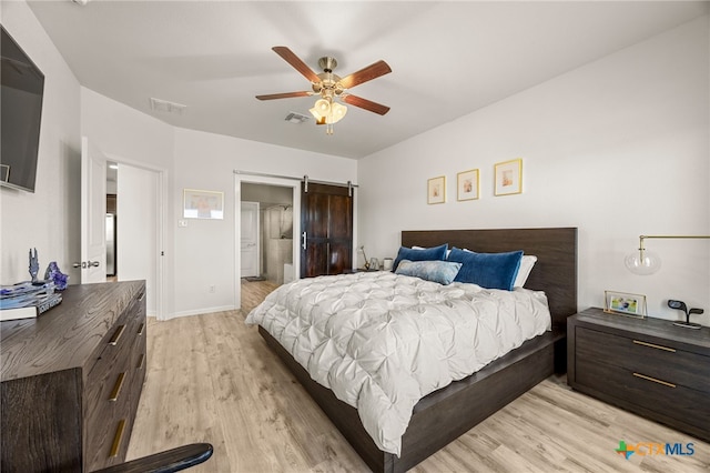 bedroom featuring ensuite bathroom, a barn door, ceiling fan, and light hardwood / wood-style flooring