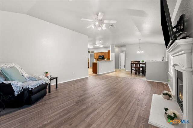 living area with light wood finished floors, ceiling fan with notable chandelier, baseboards, lofted ceiling, and visible vents