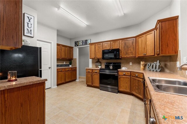 kitchen with brown cabinets, a sink, black appliances, and tasteful backsplash
