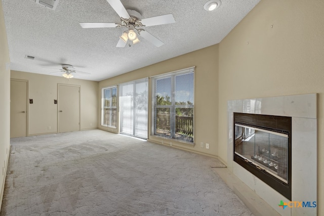 unfurnished living room featuring a tiled fireplace, ceiling fan, light colored carpet, and a textured ceiling