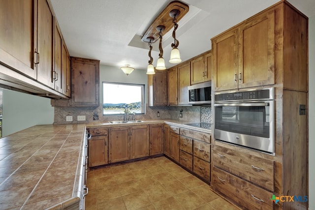 kitchen featuring tile countertops, pendant lighting, sink, decorative backsplash, and stainless steel appliances