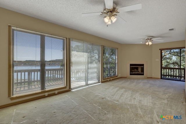 unfurnished living room featuring a textured ceiling, light colored carpet, ceiling fan, and a water view