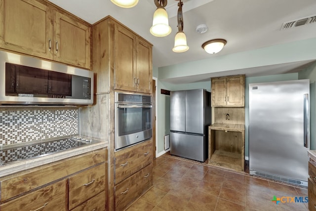 kitchen with dark tile patterned floors, appliances with stainless steel finishes, pendant lighting, and backsplash