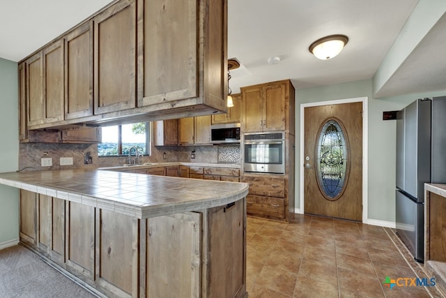 kitchen with decorative backsplash, tile countertops, stainless steel appliances, and kitchen peninsula