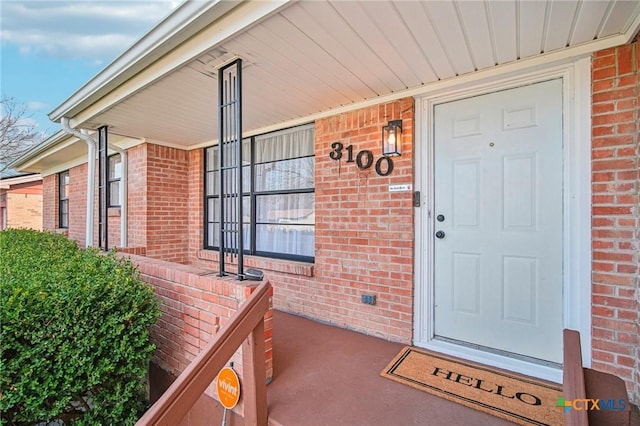 view of exterior entry featuring covered porch and brick siding