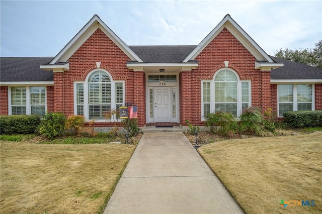 view of front of property with a front lawn, a shingled roof, and brick siding