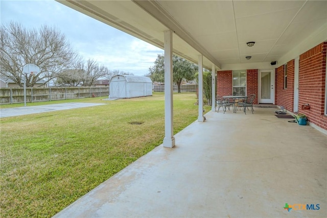 view of patio featuring an outbuilding, outdoor dining area, a fenced backyard, and a storage shed