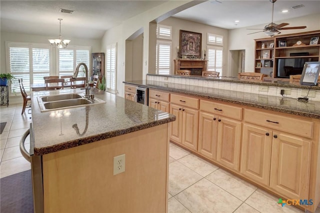 kitchen with an island with sink, decorative light fixtures, light brown cabinets, a sink, and light tile patterned flooring