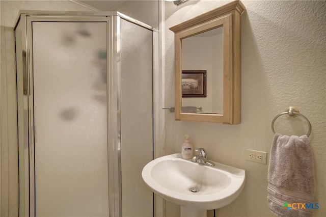 bathroom featuring a textured wall, a stall shower, and a sink