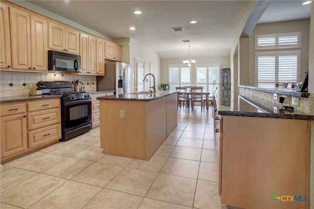 kitchen featuring pendant lighting, a center island with sink, light tile patterned flooring, dark stone countertops, and black appliances