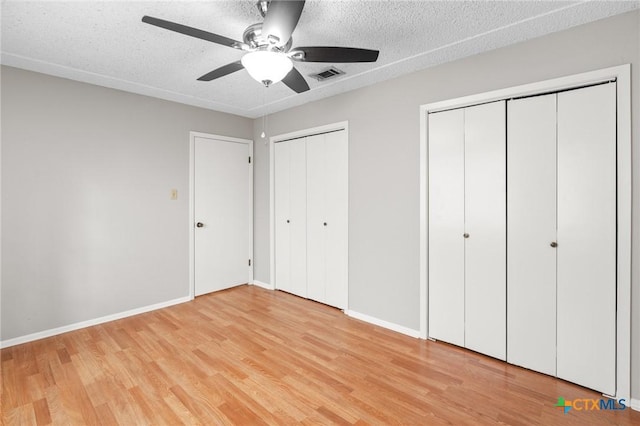 unfurnished bedroom featuring ceiling fan, two closets, a textured ceiling, and light wood-type flooring