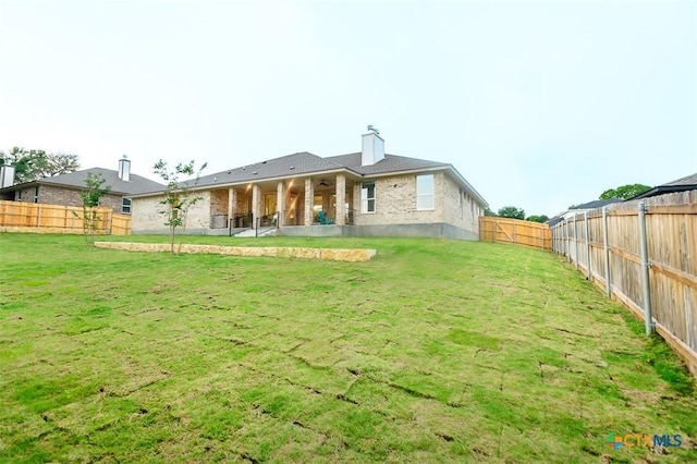 rear view of property with a lawn, a fenced backyard, ceiling fan, and a chimney