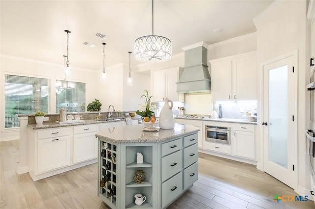 kitchen featuring custom exhaust hood, oven, a center island, a chandelier, and a sink