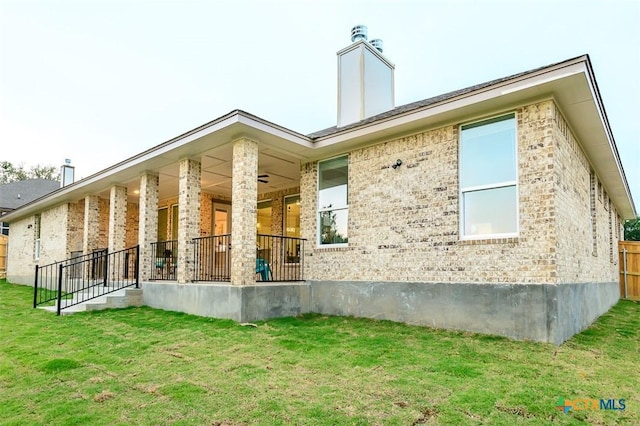 rear view of house featuring brick siding, a lawn, a chimney, and a porch
