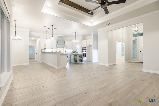 unfurnished living room featuring crown molding, light wood-style flooring, a raised ceiling, and ceiling fan with notable chandelier