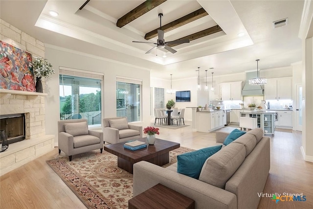living area with visible vents, ornamental molding, a stone fireplace, a raised ceiling, and ceiling fan with notable chandelier