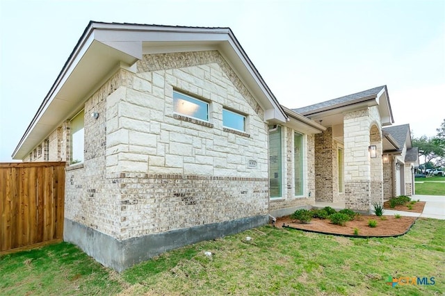 view of side of property with a lawn, brick siding, fence, and stone siding