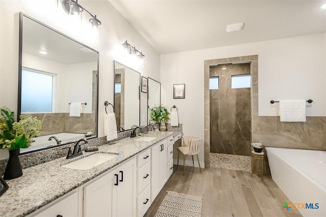bathroom featuring double vanity, a soaking tub, a sink, and wood finished floors