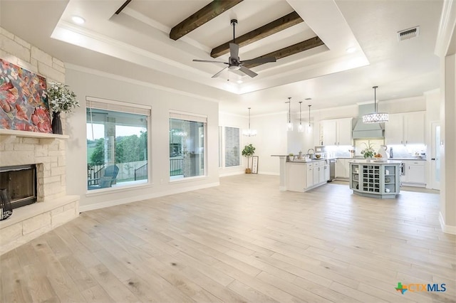 unfurnished living room featuring crown molding, light wood-style floors, a stone fireplace, a raised ceiling, and ceiling fan with notable chandelier