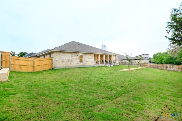 rear view of house featuring a yard, brick siding, a chimney, and a fenced backyard