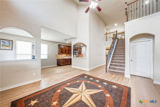 entryway featuring ceiling fan, light hardwood / wood-style flooring, and a towering ceiling