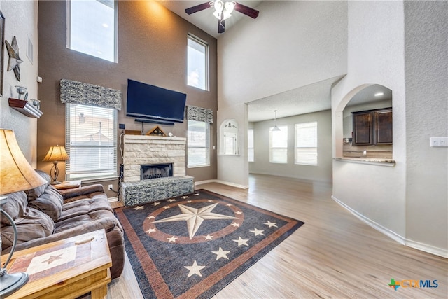 living room with ceiling fan, a high ceiling, plenty of natural light, and a stone fireplace