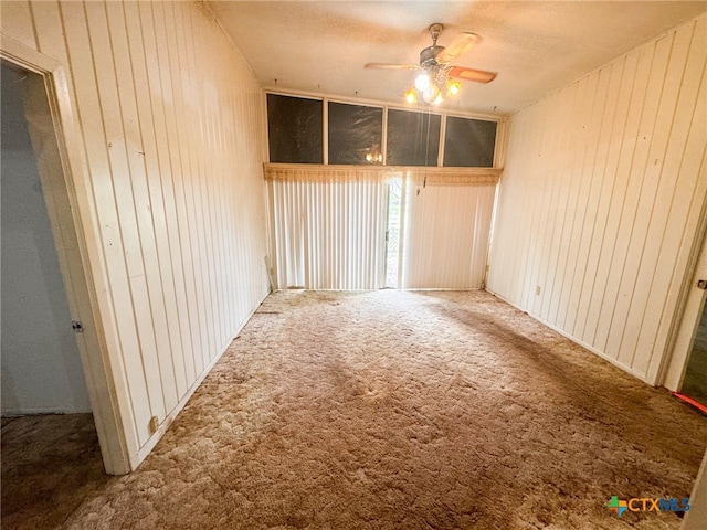 carpeted empty room featuring a textured ceiling, wood walls, and ceiling fan