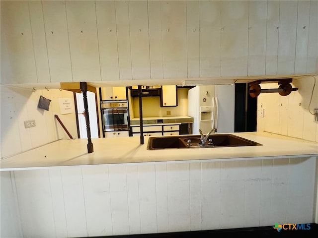 kitchen featuring kitchen peninsula, white fridge with ice dispenser, sink, and oven