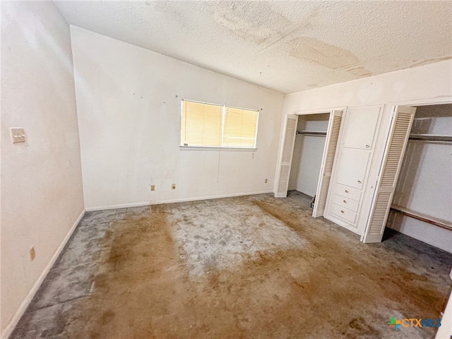 unfurnished bedroom with concrete floors, a textured ceiling, and two closets