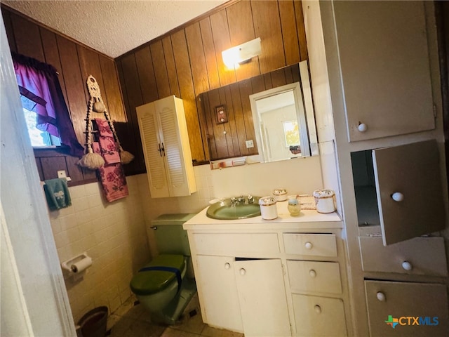 bathroom featuring wooden walls, vanity, a textured ceiling, and toilet