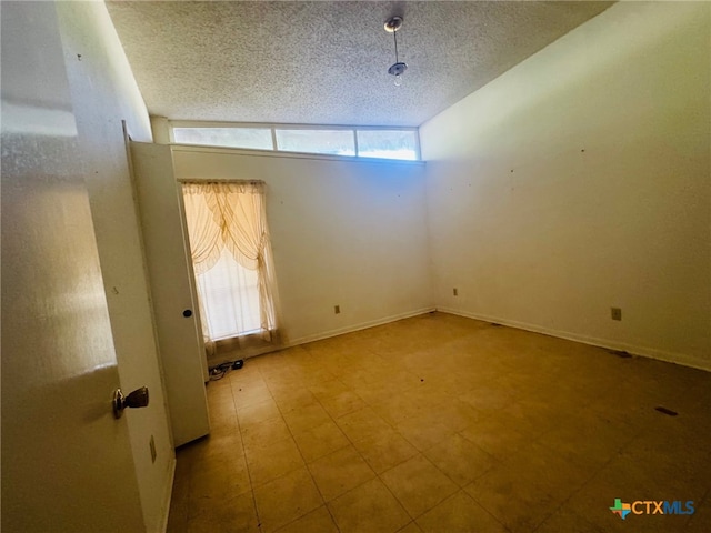 spare room featuring lofted ceiling, a textured ceiling, and a healthy amount of sunlight