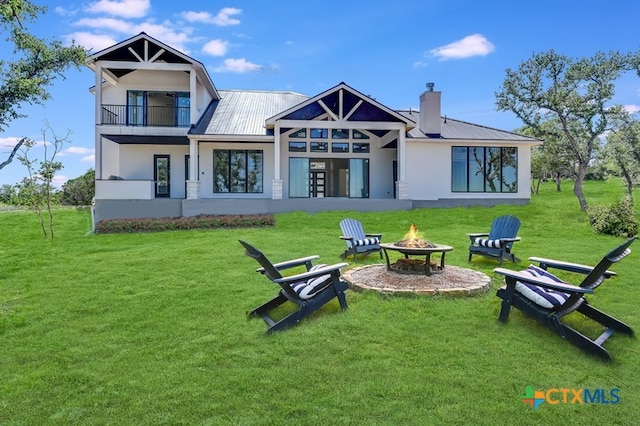 rear view of property with a yard, a balcony, and an outdoor fire pit