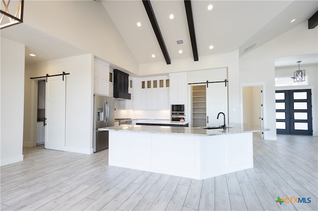 kitchen with a barn door, high vaulted ceiling, stainless steel appliances, and a large island with sink