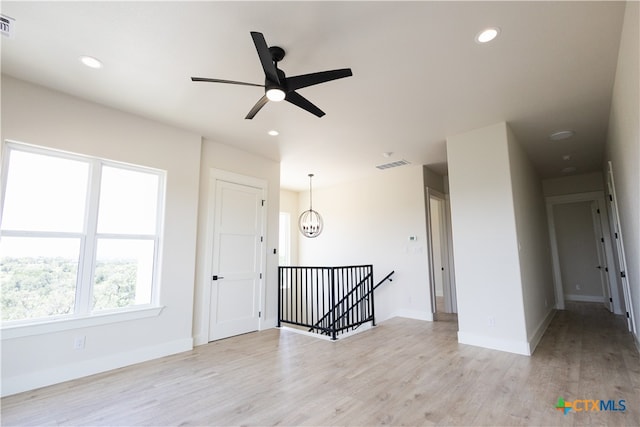 spare room featuring ceiling fan with notable chandelier and light hardwood / wood-style floors