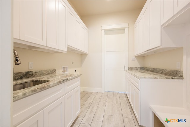 kitchen with white cabinetry, sink, light stone countertops, and light hardwood / wood-style flooring