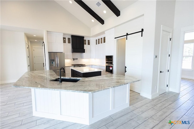 1193 Country Pike, Canyon Lake, TX 78133 - kitchen featuring appliances with stainless steel finishes, a large island, a barn door, beam ceiling, and light wood-style flooring