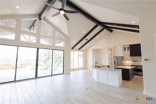 kitchen featuring appliances with stainless steel finishes, light stone counters, high vaulted ceiling, beamed ceiling, and a large island