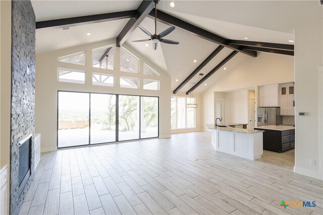 1193 Country Pike, Canyon Lake, TX 78133 - unfurnished living room featuring beamed ceiling, high vaulted ceiling, ceiling fan, a fireplace, and light wood-style floors