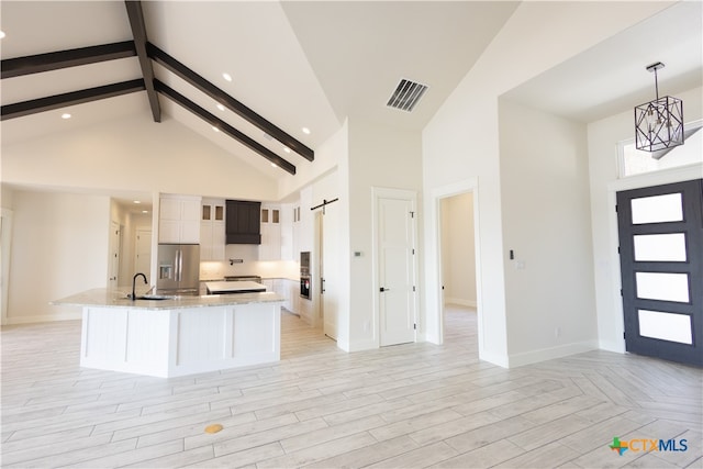 kitchen featuring high vaulted ceiling, stainless steel fridge, a barn door, light stone countertops, and decorative light fixtures