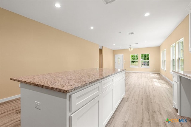1700 Proctor Ave, Waco, TX 76708 - kitchen with light wood-type flooring, a ceiling fan, a kitchen island, light stone counters, and white cabinetry