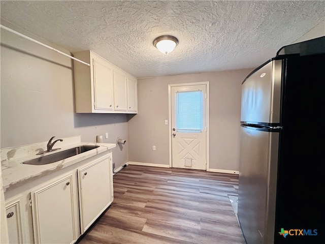 laundry room featuring cabinets, a textured ceiling, sink, washer hookup, and light hardwood / wood-style flooring