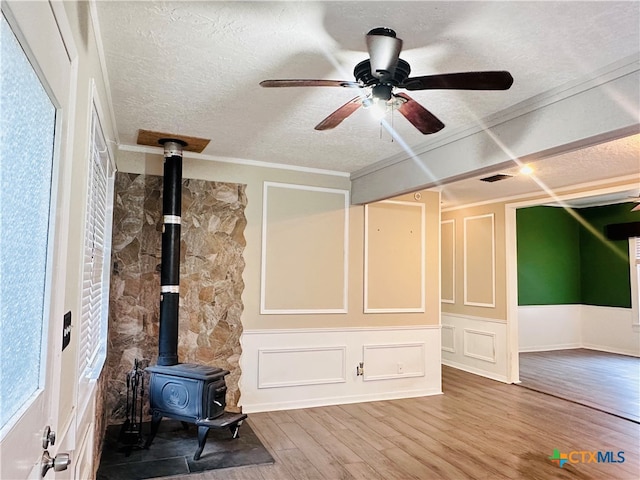 unfurnished living room featuring wood-type flooring, a wood stove, a textured ceiling, ornamental molding, and ceiling fan